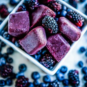 Blue elderberry smoothie cubes in a square bowl with berries.