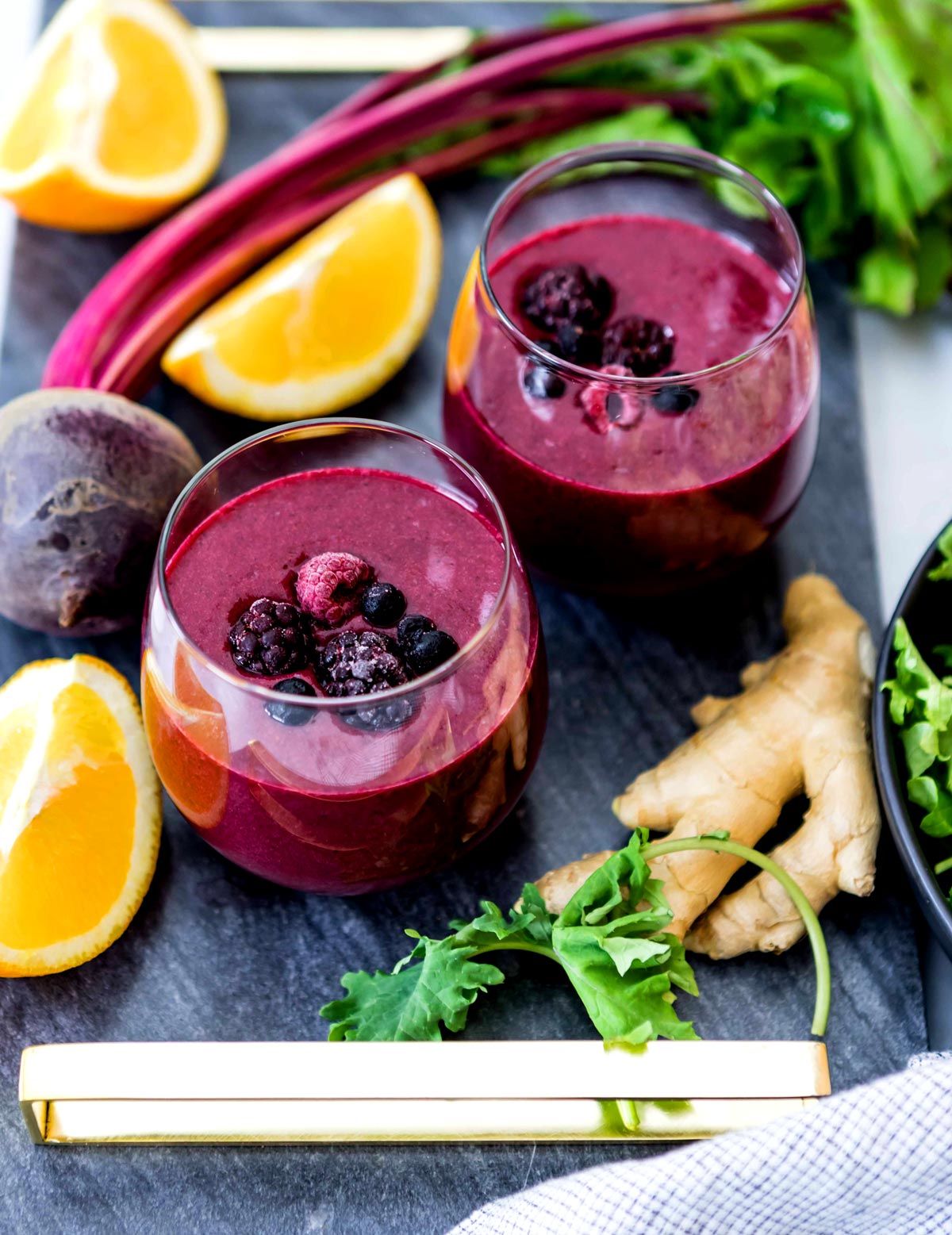 Two anti-inflammatory berry smoothies surrounded by anti inflammatory ingredients such as lemon, beets, ginger and kale.