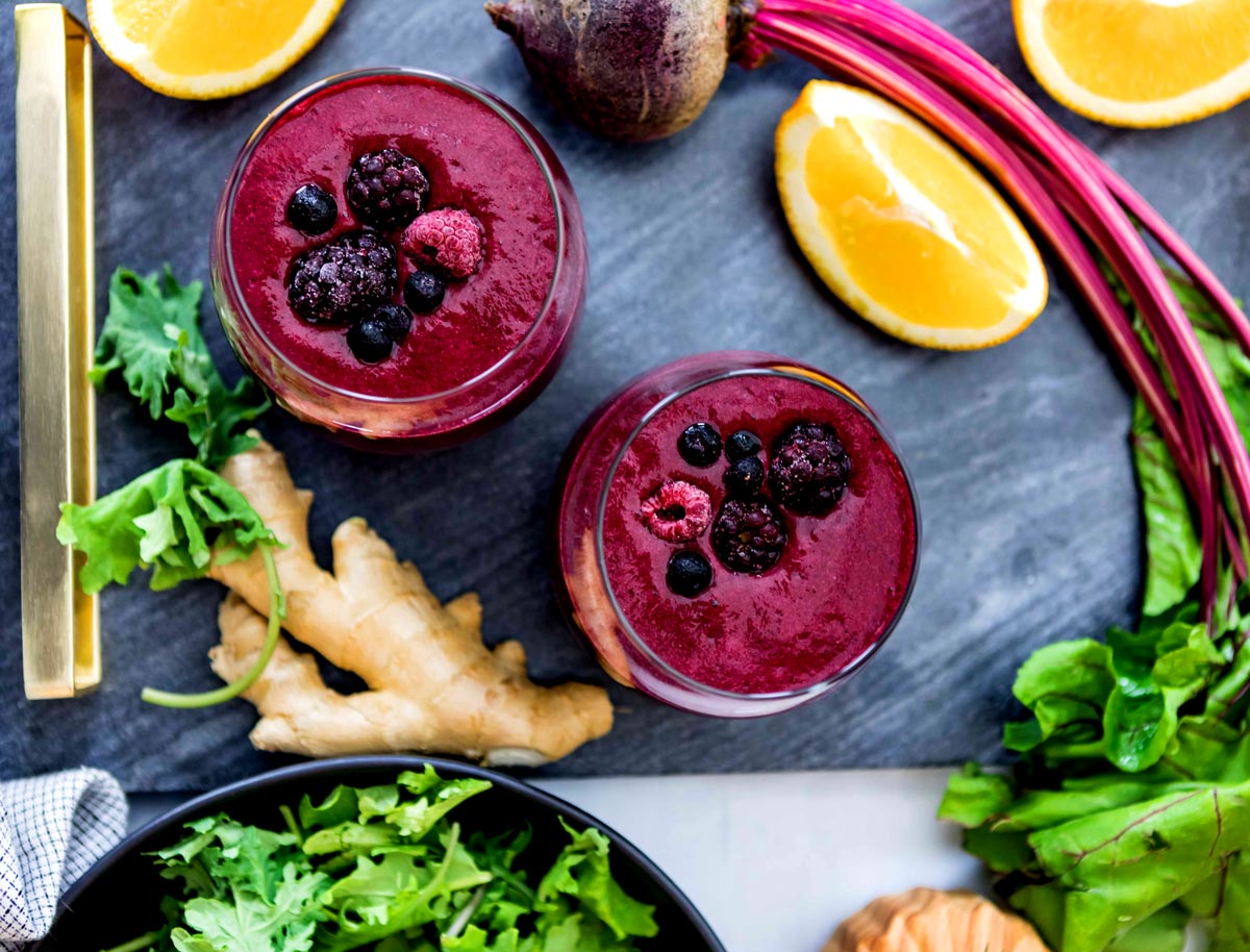 Two anti-inflammatory berry smoothies surrounded by anti inflammatory ingredients such as lemon, beets, ginger and kale.