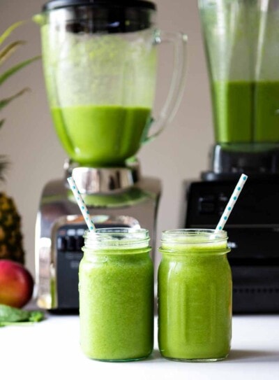 Glass of green smoothie in front of Oster blender and Vitamix blender.