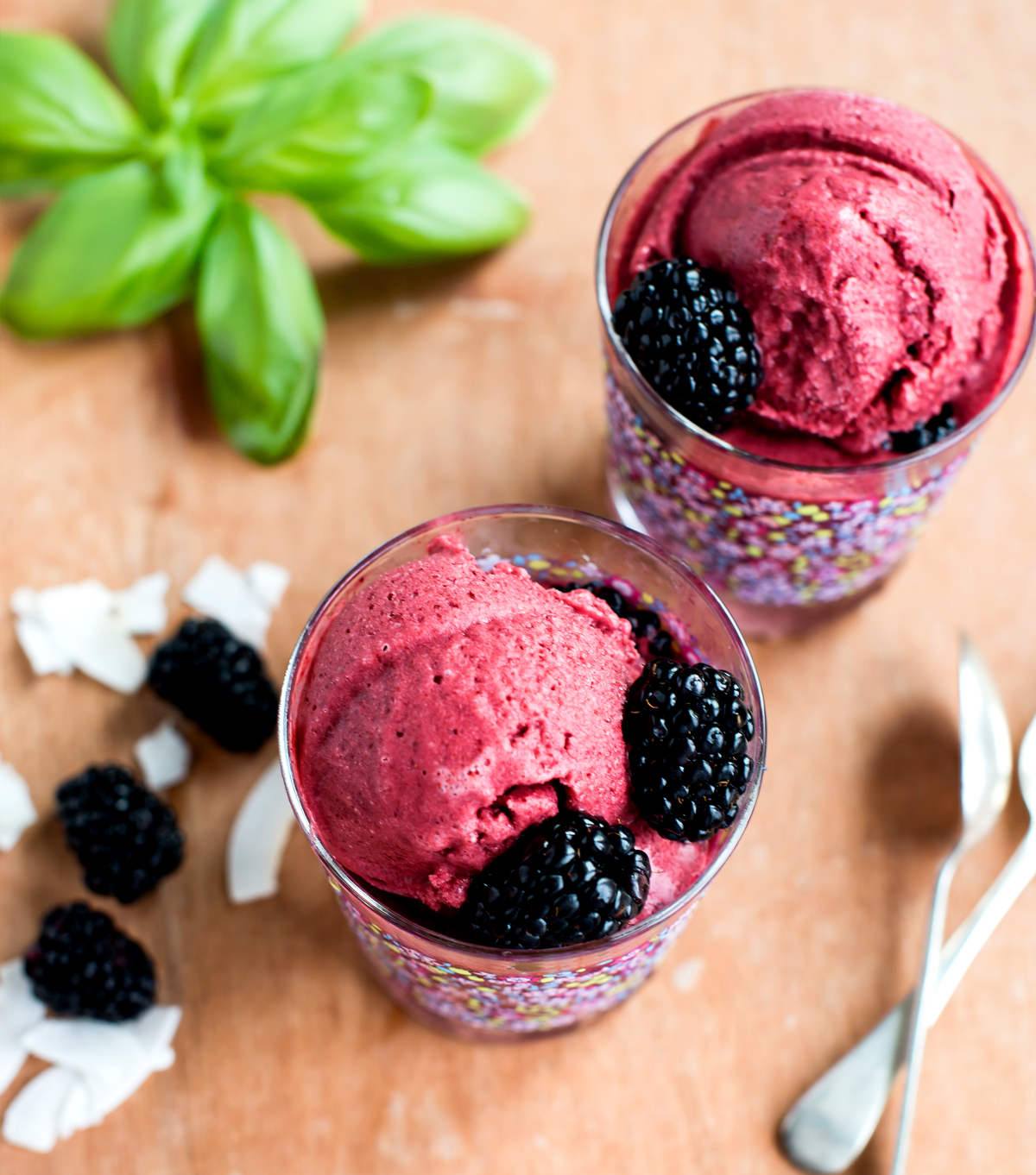 Two glasses filled with blackberry coconut sorbet, with blackberries, coconut flakes, and silverware.