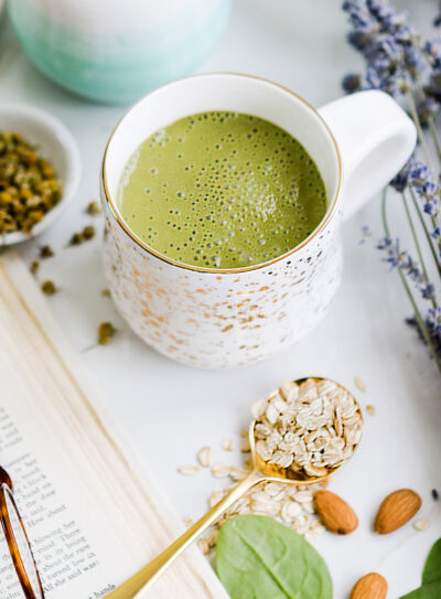 Green bedtime smoothie in a white mug surrounded by lavender, almonds, tea, and spinach.