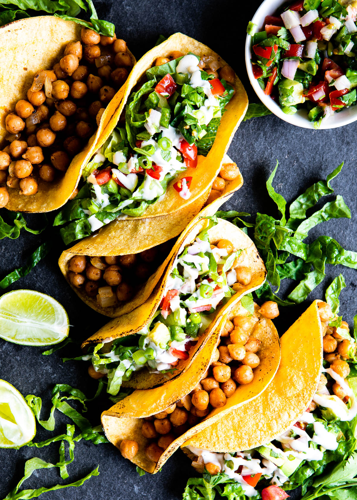 A line of healthy chickpea tacos with every other one topped with fresh toppings.