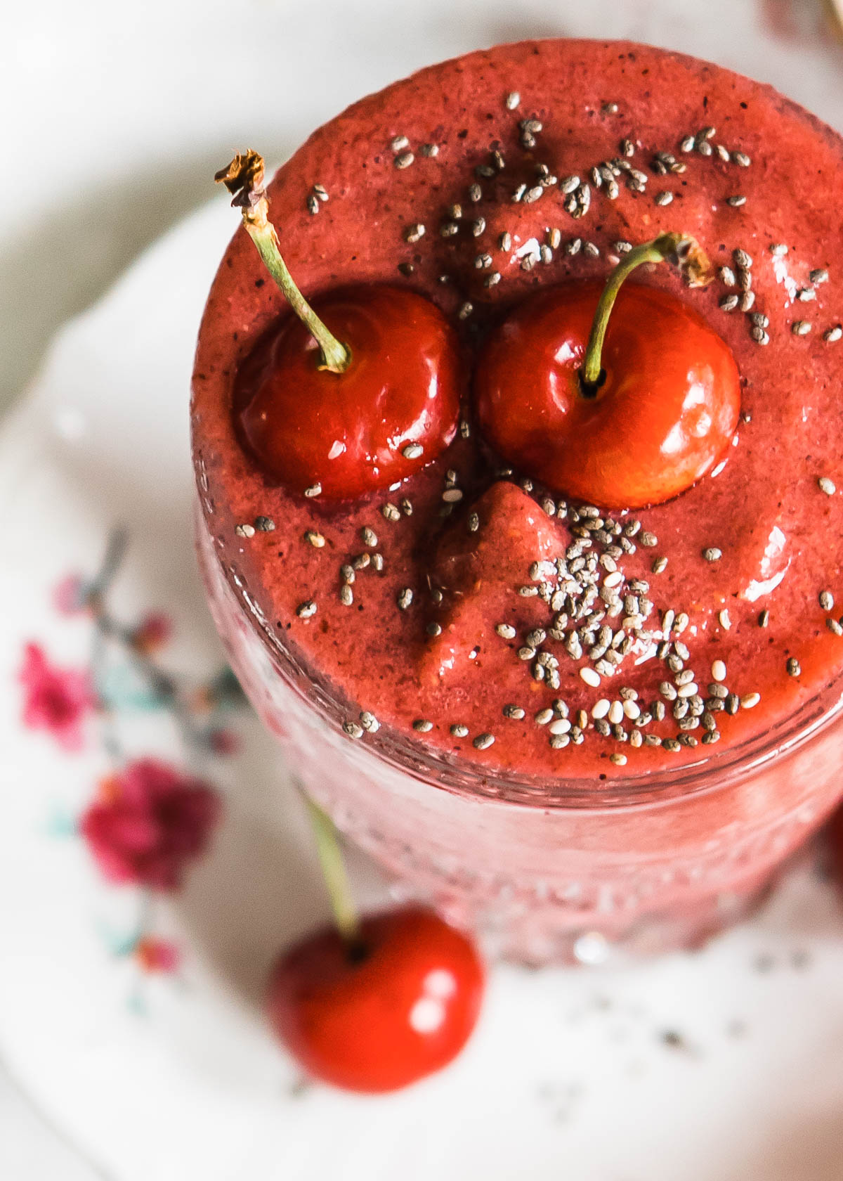A glass of cherry smoothie topped with a whole cherry and chia seeds.