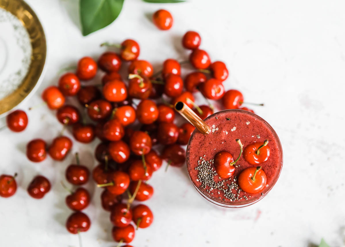 A glass of power cherry smoothie on countertop, surrounded by fresh cherries for garnish.