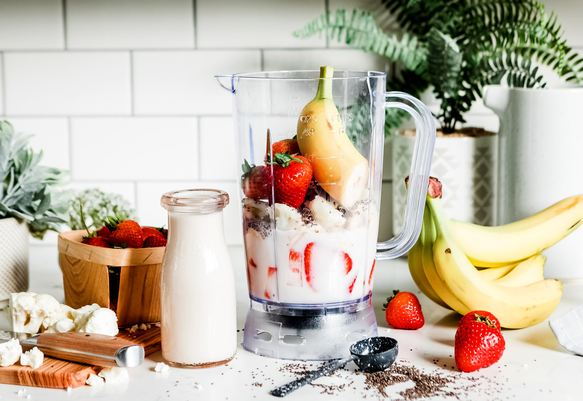 Blender container filled with strawberries, bananas and cauliflower to make a smoothie.