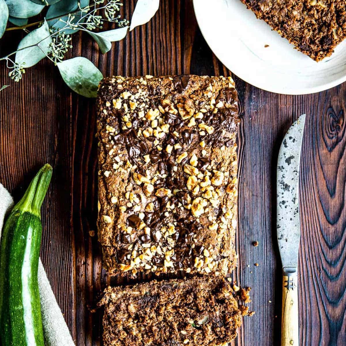 Loaf of healthy zucchini bread with end sliced off next to a knife and a whole zucchini.