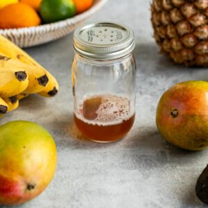 Fruit fly trap in a jar surrounded by fruit.