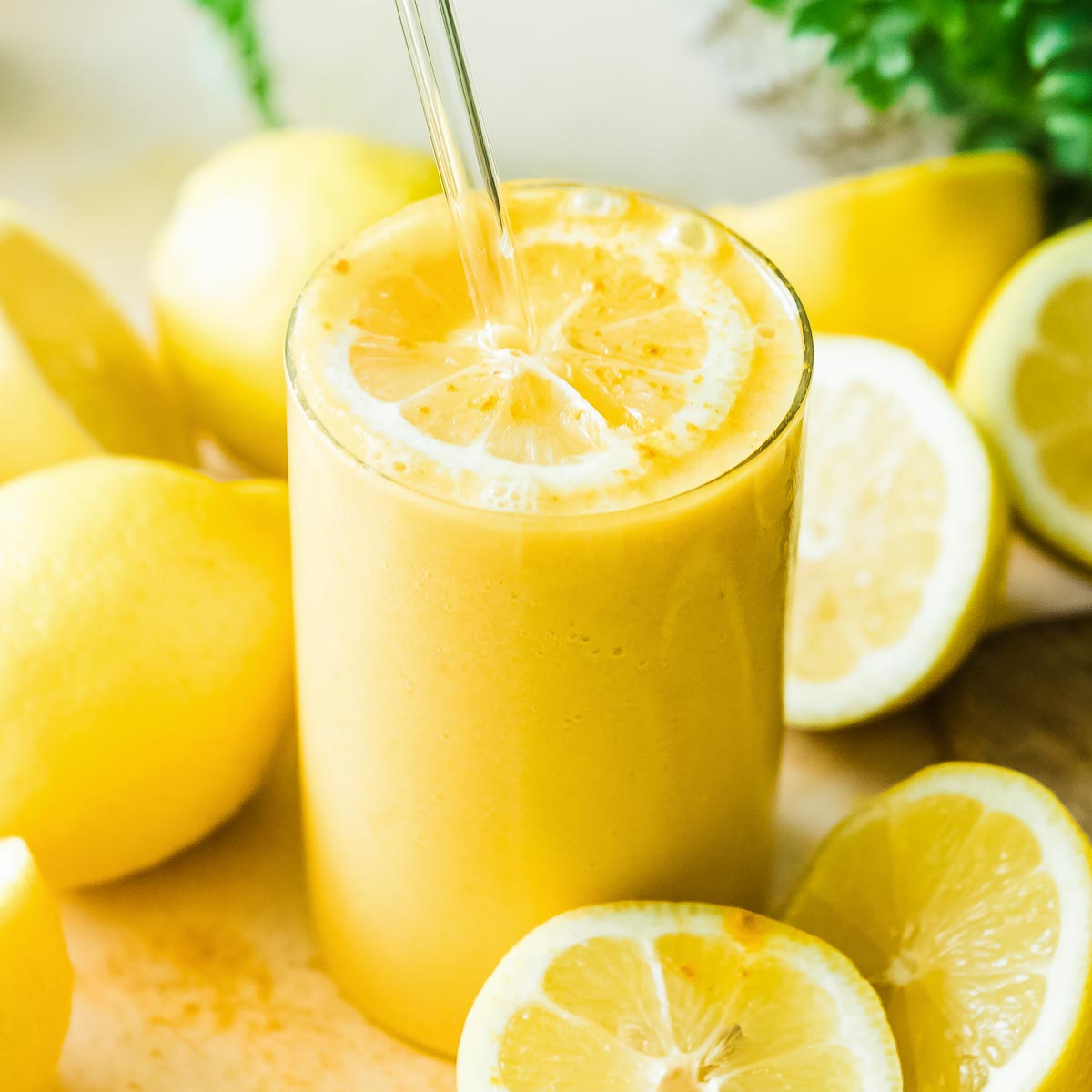 Lemon smoothie in a glass with straw surrounded by lemons.