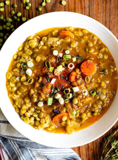 Vegetarian split pea soup in a white bowl next to a spoon on a blue striped tea towel.