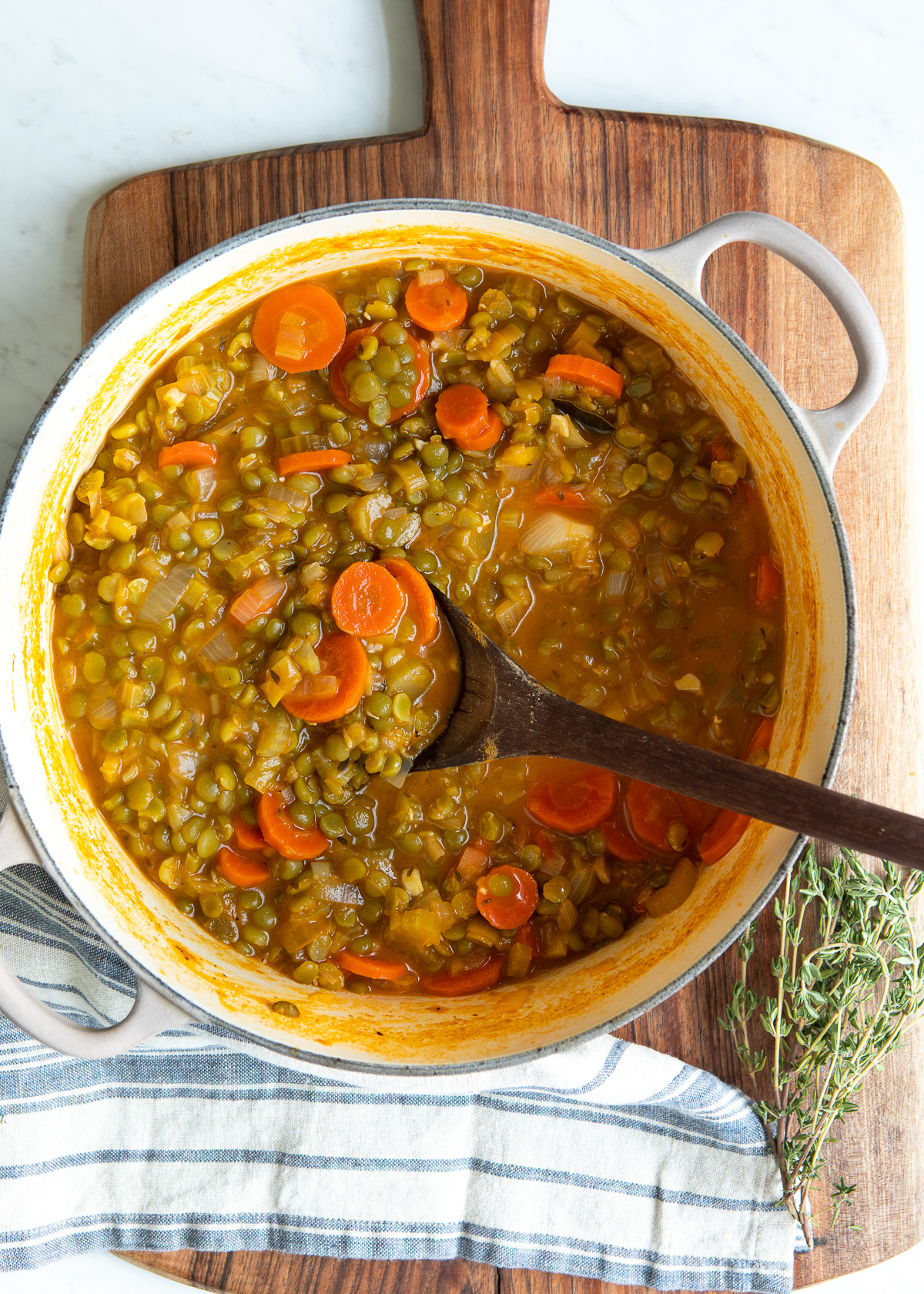White pot of vegetarian split pea soup is being stirred with a wooden spoon.