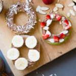 Apple donuts with various toppings on a wooden board.