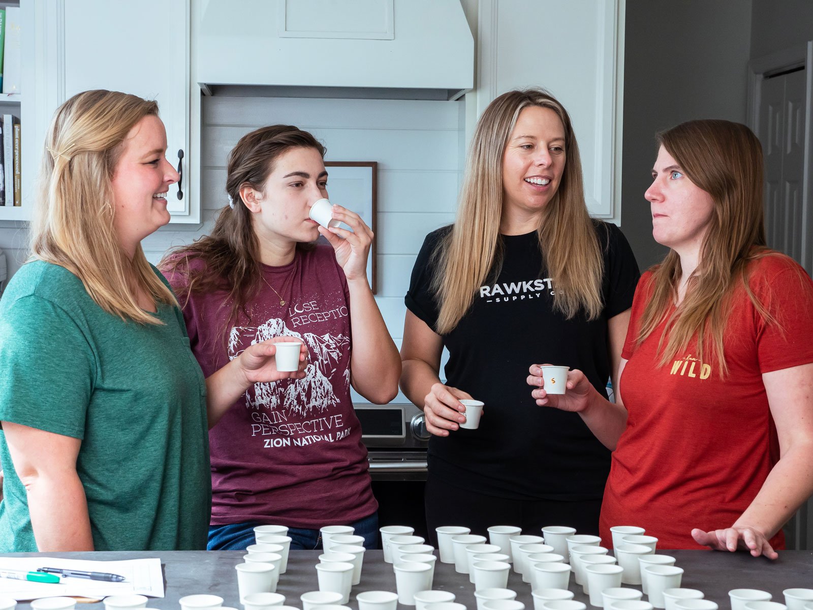 Women taste testing almond milk brands in kitchen.