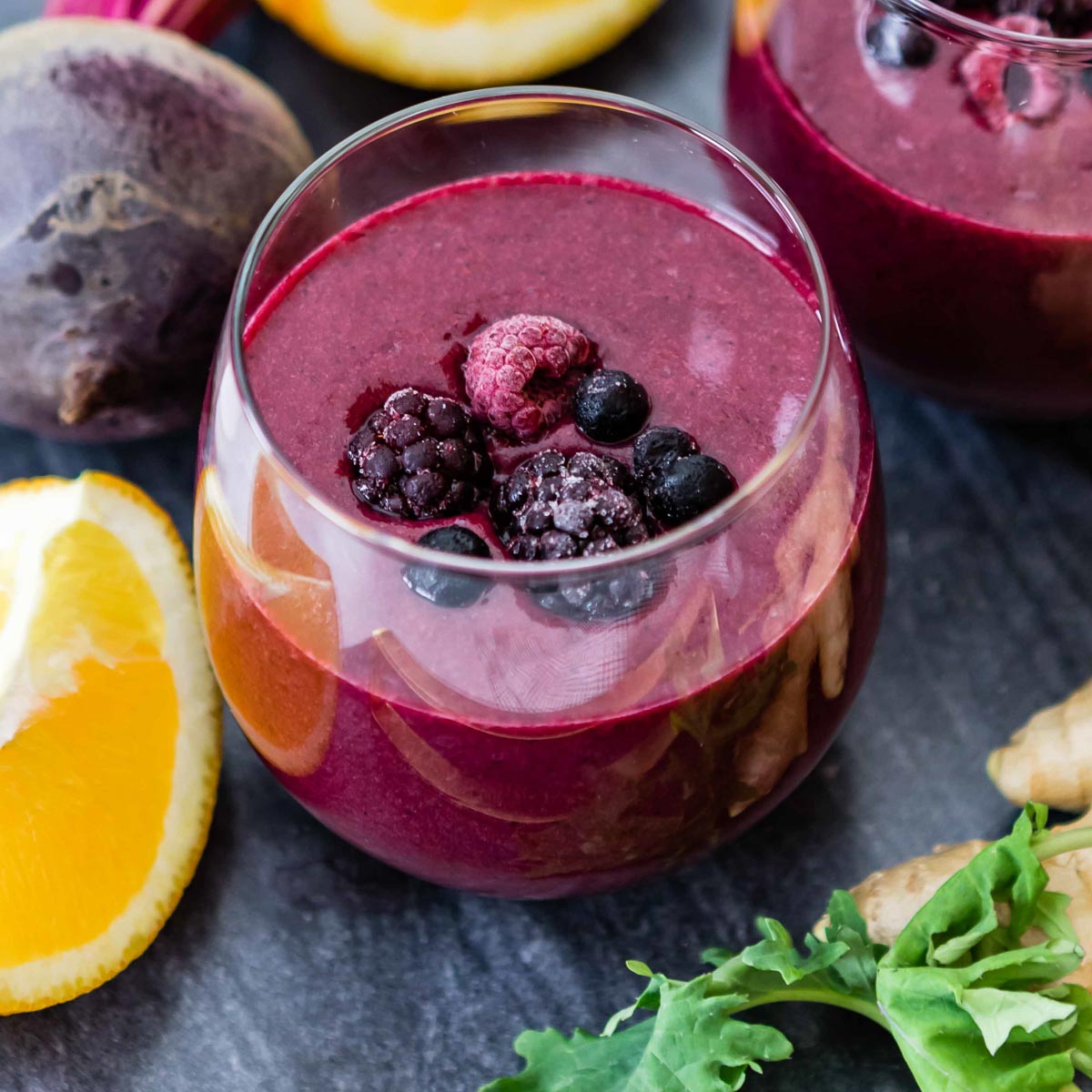 glass with purple smoothie in it, topped with frozen fruit.