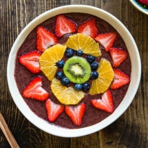 Smoothie bowl with fruit arranged in a flower pattern on top.