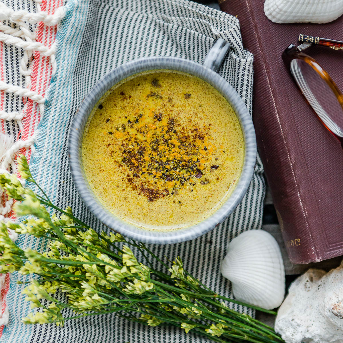 Mug of golden milk topped with ground turmeric and cracked black pepper on a wooden tray with fresh spring flowers.