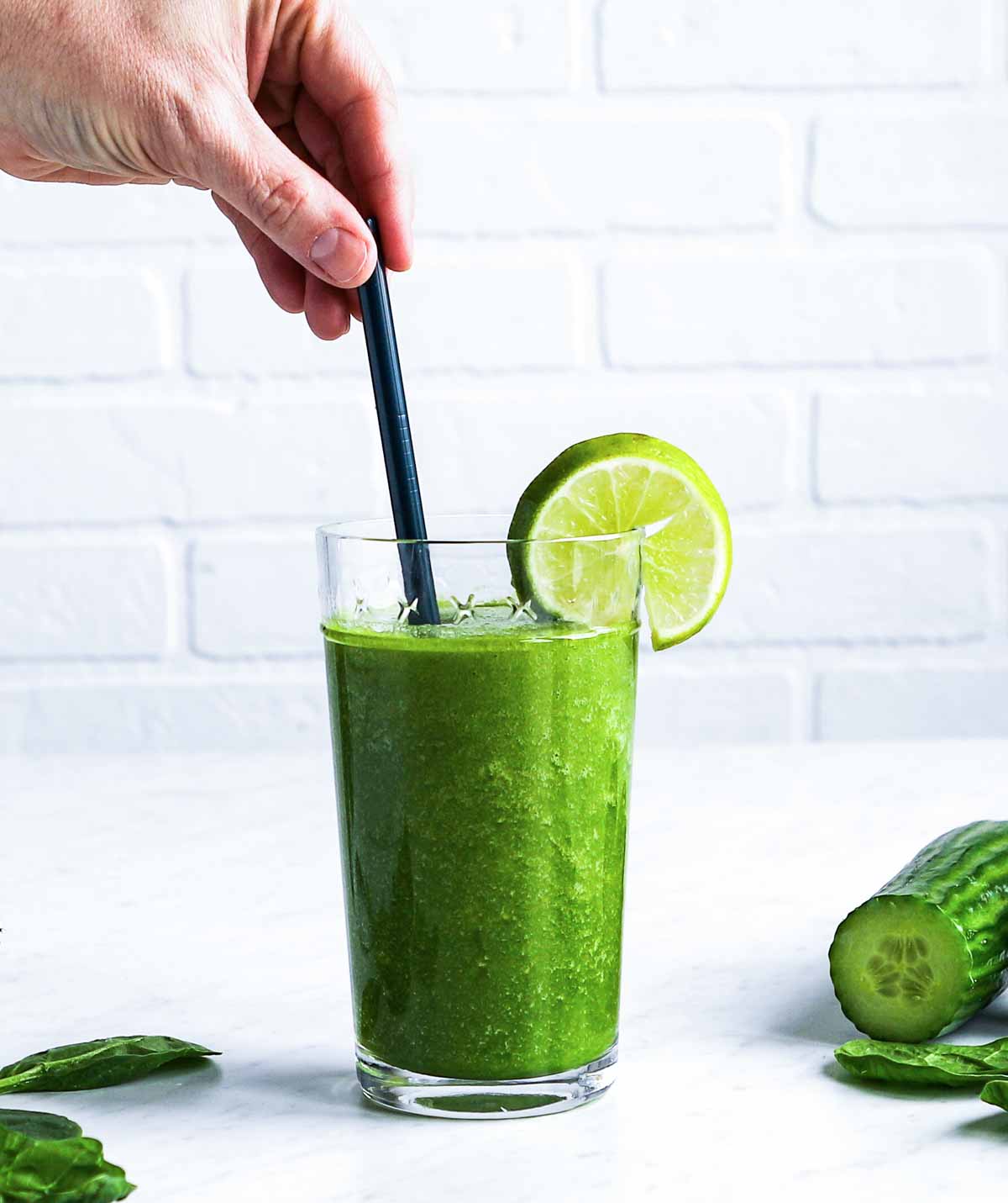 Person adding a straw to a green smoothie in a tall glass with a lime wedge.
