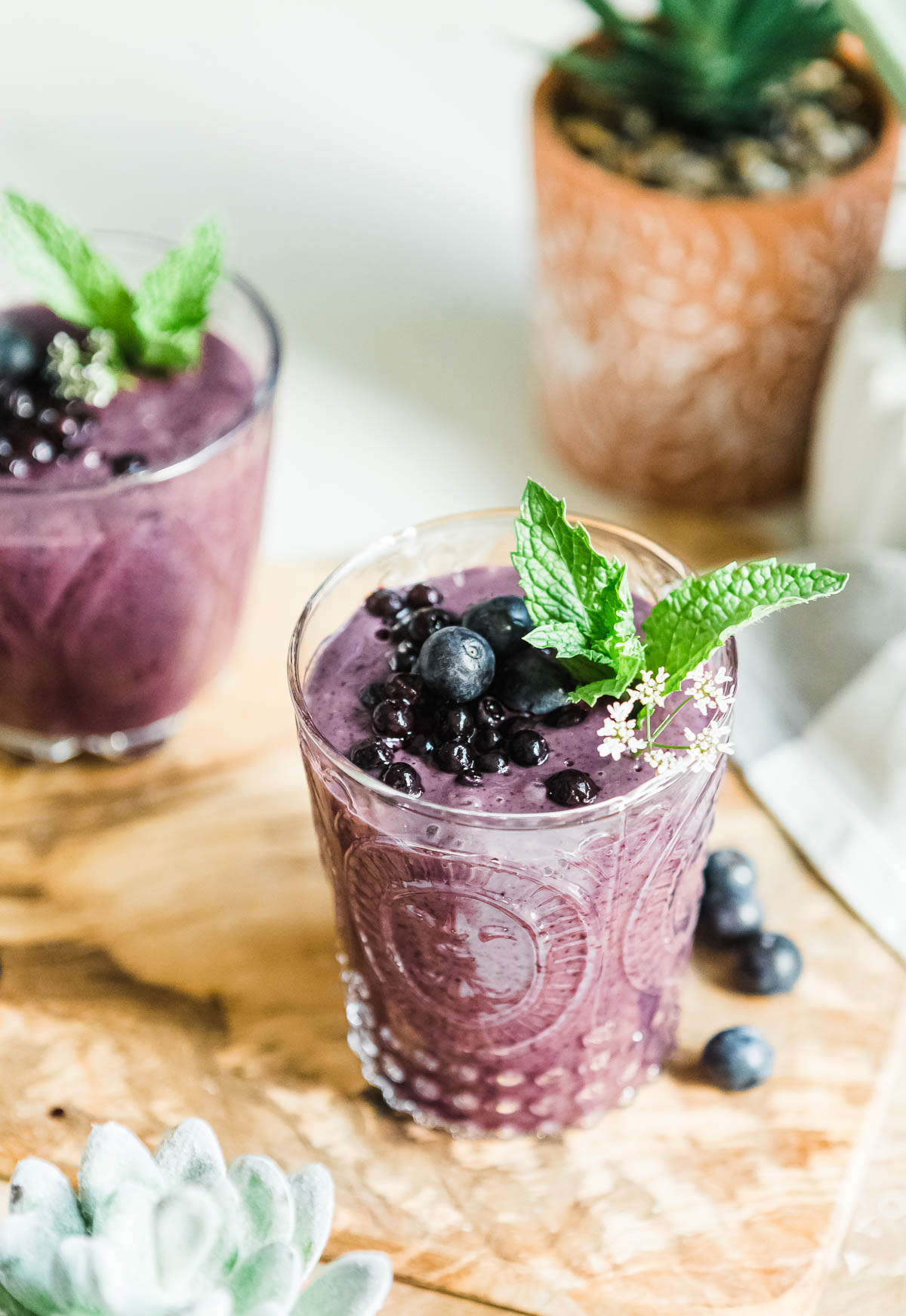 Two healthy blueberry smoothies topped with fresh fruit and mint sprigs.