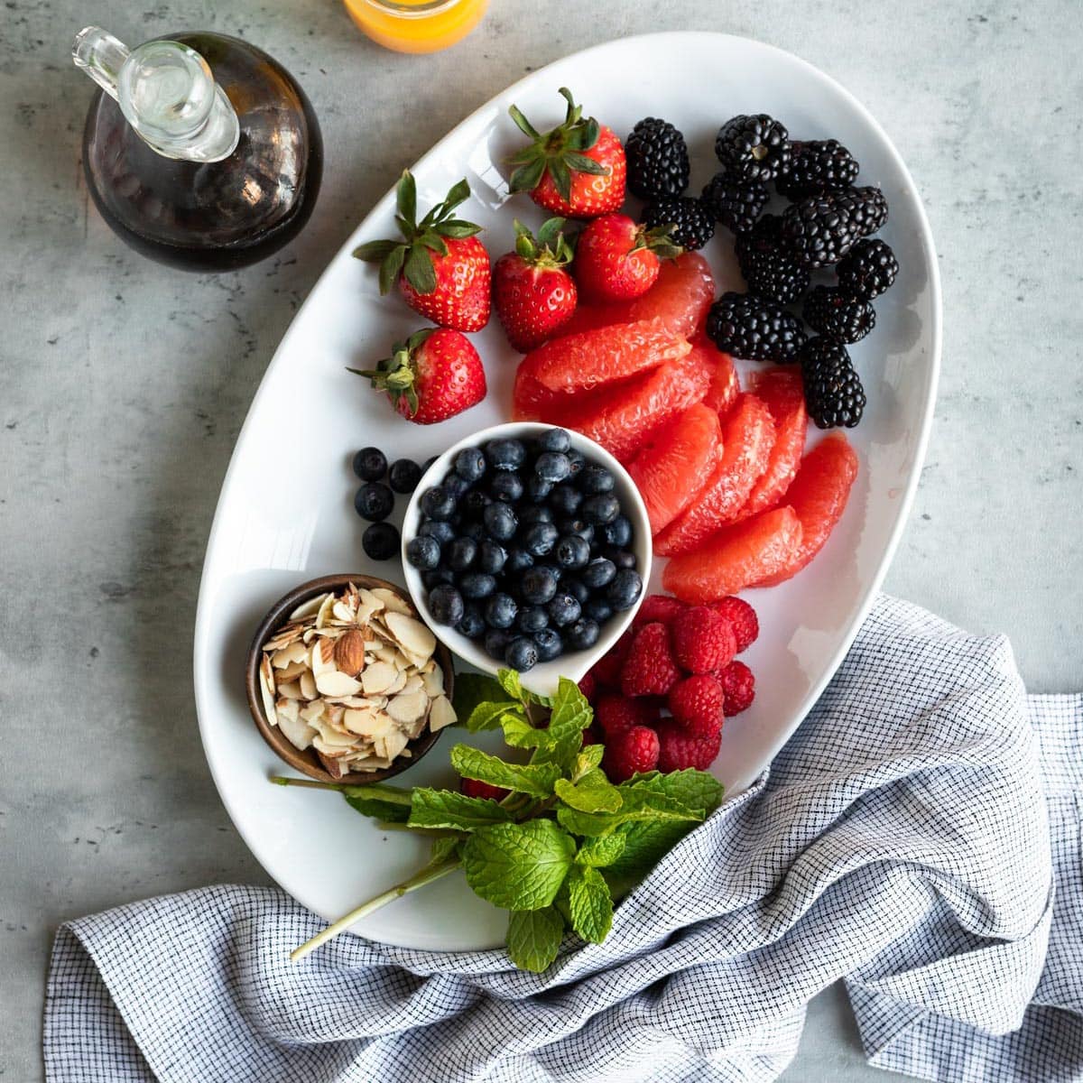 white platter of berries, grapefruit, sliced almonds and fresh mint to serve at a healthy brunch.