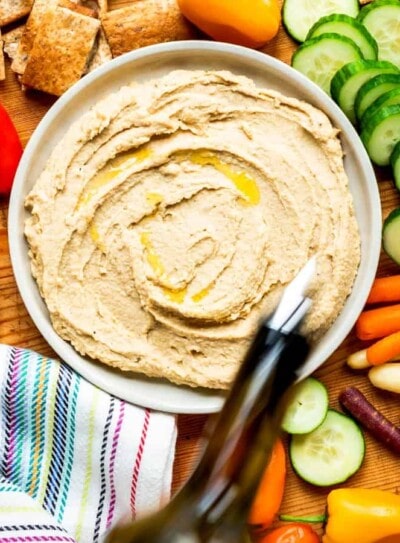 Bowl of homemade hummus surrounded by vegetables.
