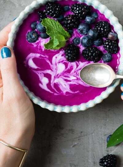 Person holding a spoon over a bright purple smoothie bowl with berries.
