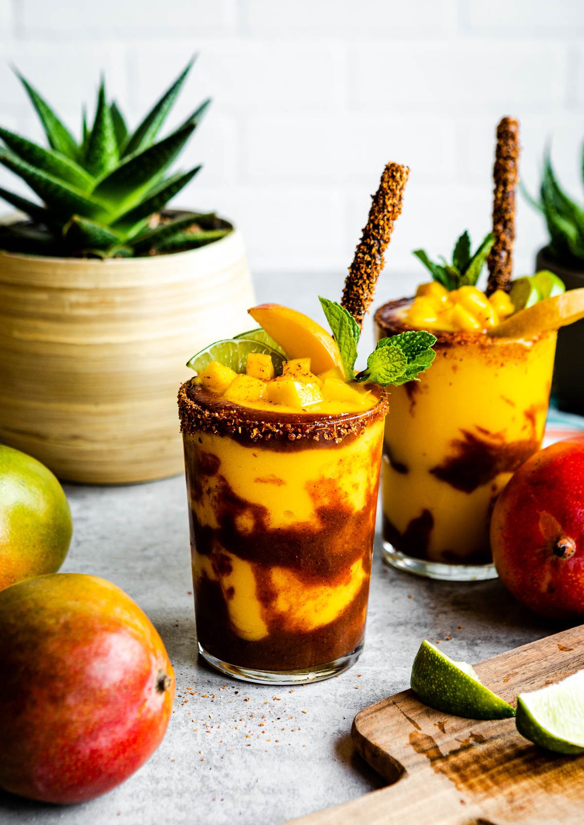 Mangonada recipe ready to serve in 2 glasses topped with mango and tamarind straws.