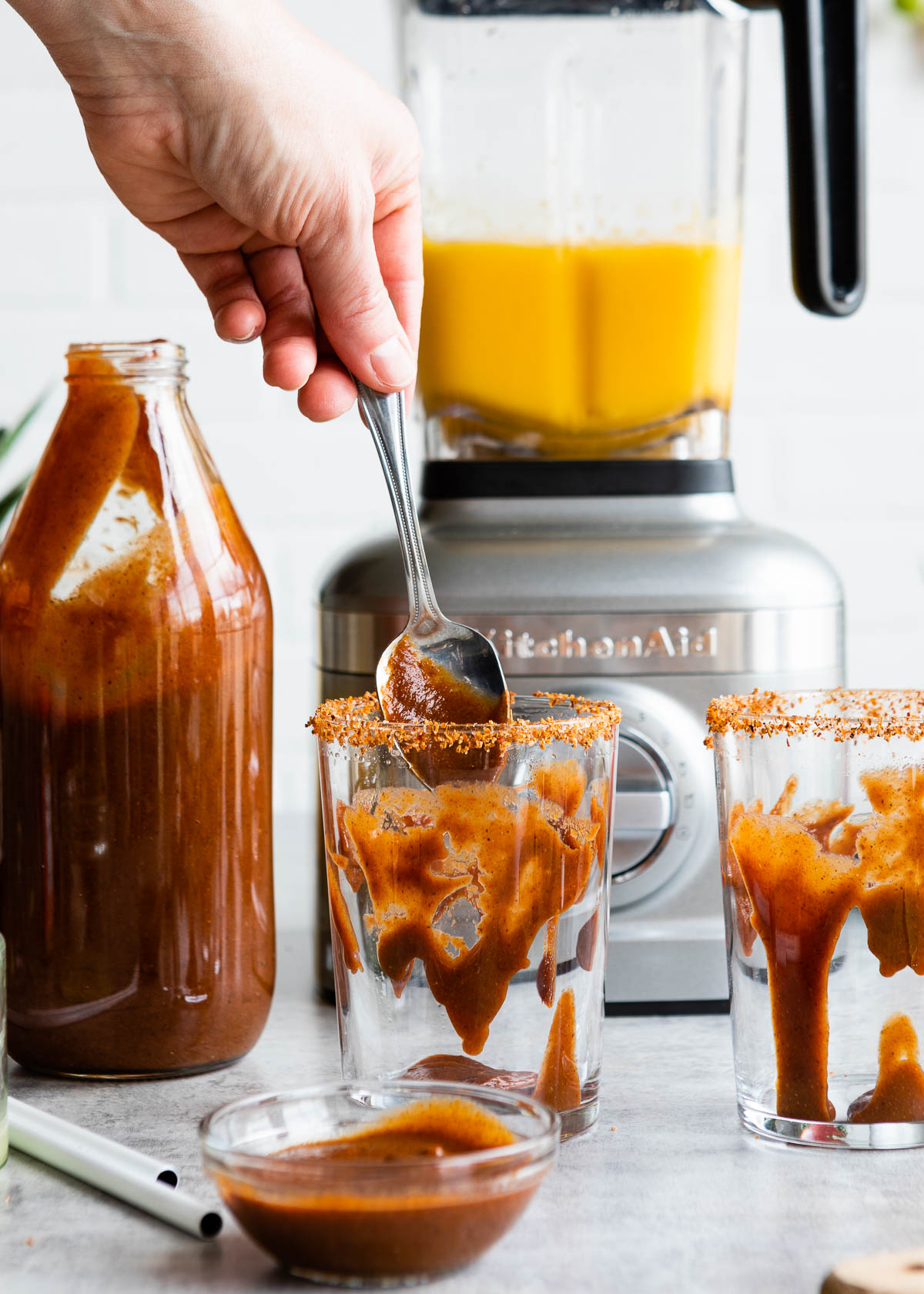 Chamoy sauce being smeared onto the inside of a clear glass, using a spoon.