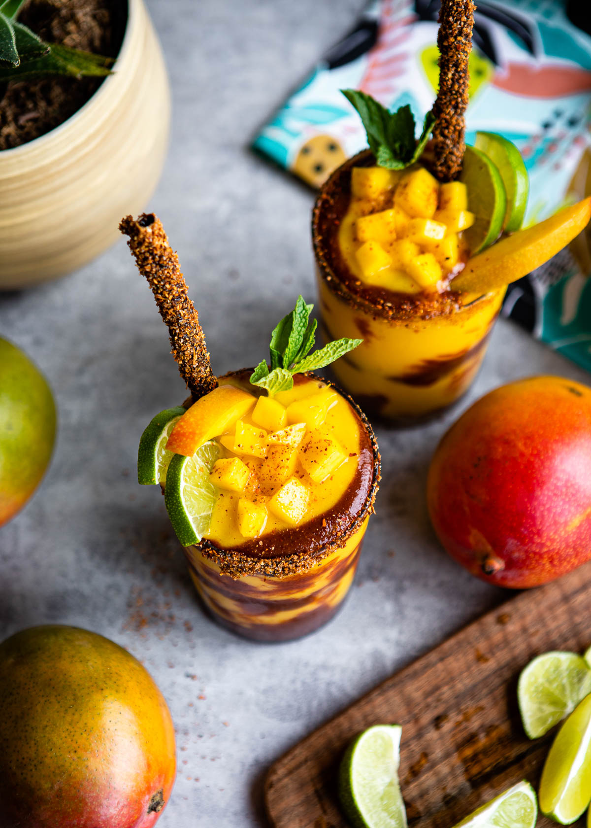 Mangonada recipe in two glasses topped with fruit and tamarind straws.