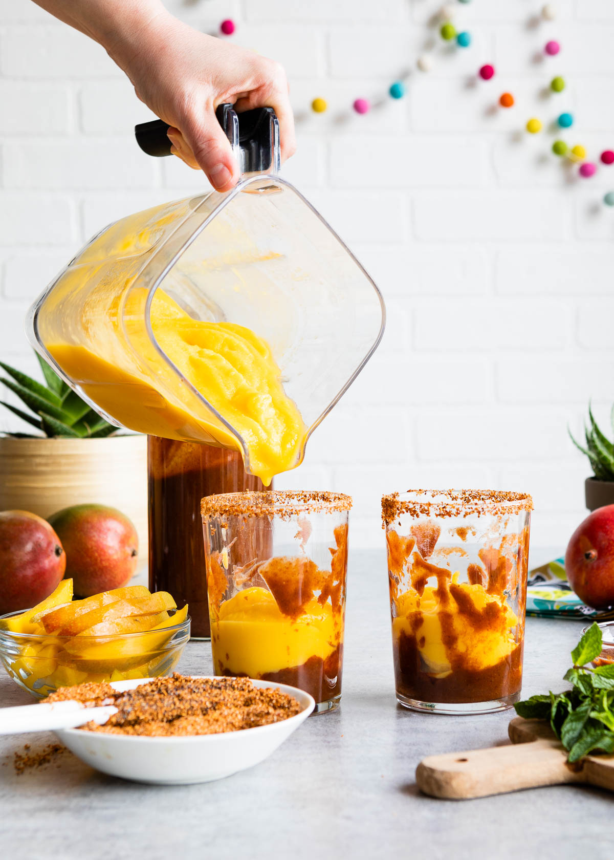 A blender filled with Mexican mangonada being poured into two clear glasses.