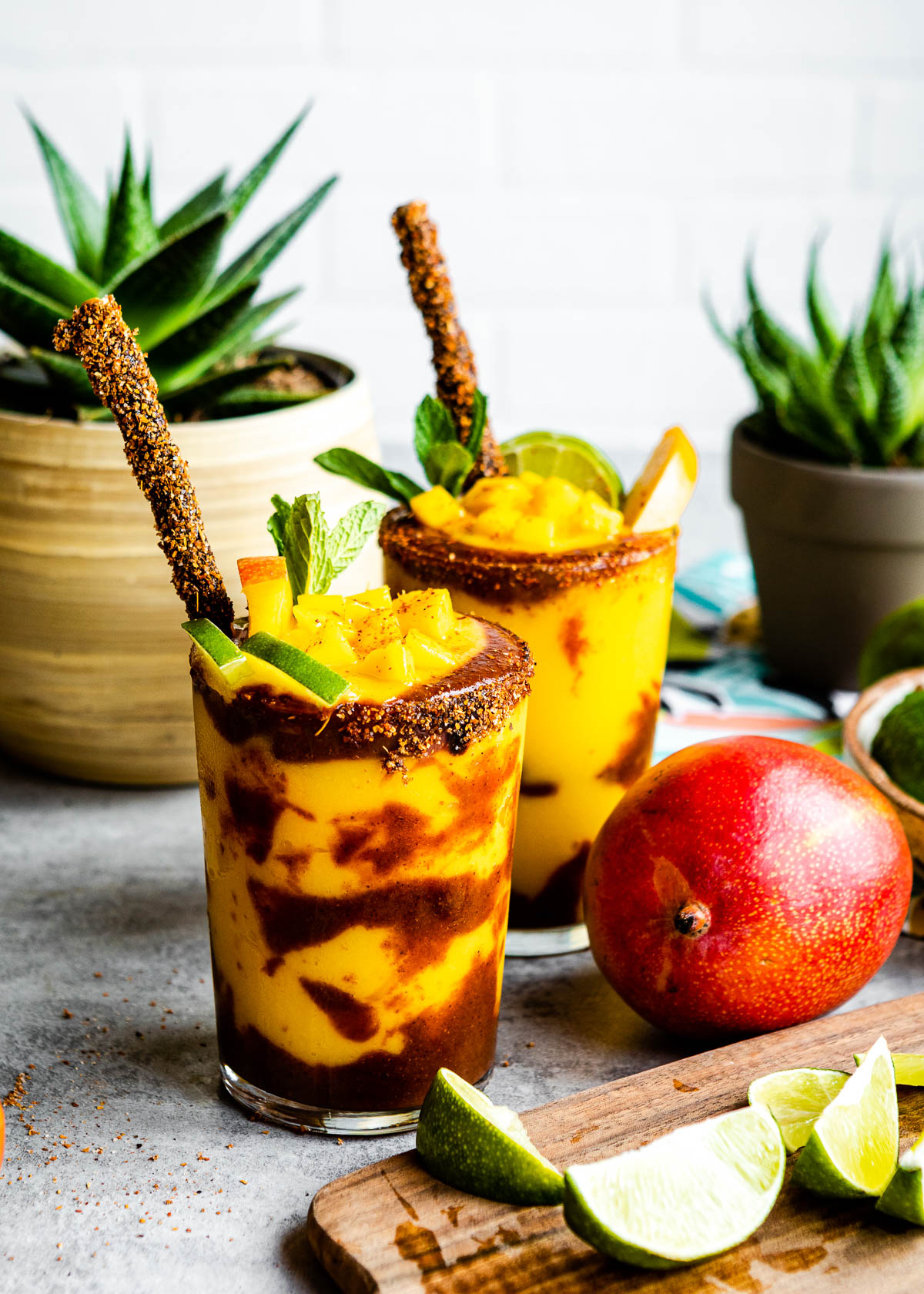 Mangonada recipe in two glasses topped with fruit and tamarind straws.