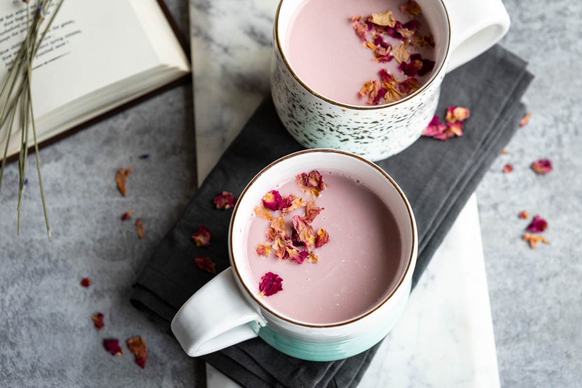 Pink moon milk in two mugs on a serving tray, surrounded by dried flowers and an open book.