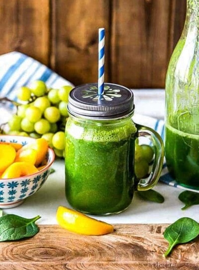 green smoothie in a glass jar with a daisy cut lid and a paper straw.