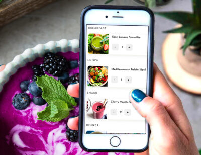 Holding a phone showing plant-based meal planner recipes.