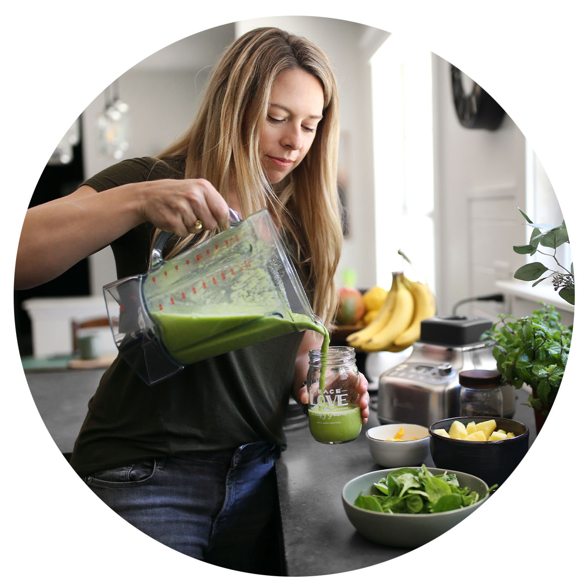 Woman pouring a Green smoothie from a blender container and a bright and open kitchen.