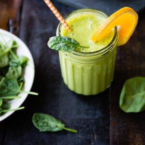 Orange spinach banana smoothie topped with an orange slice.
