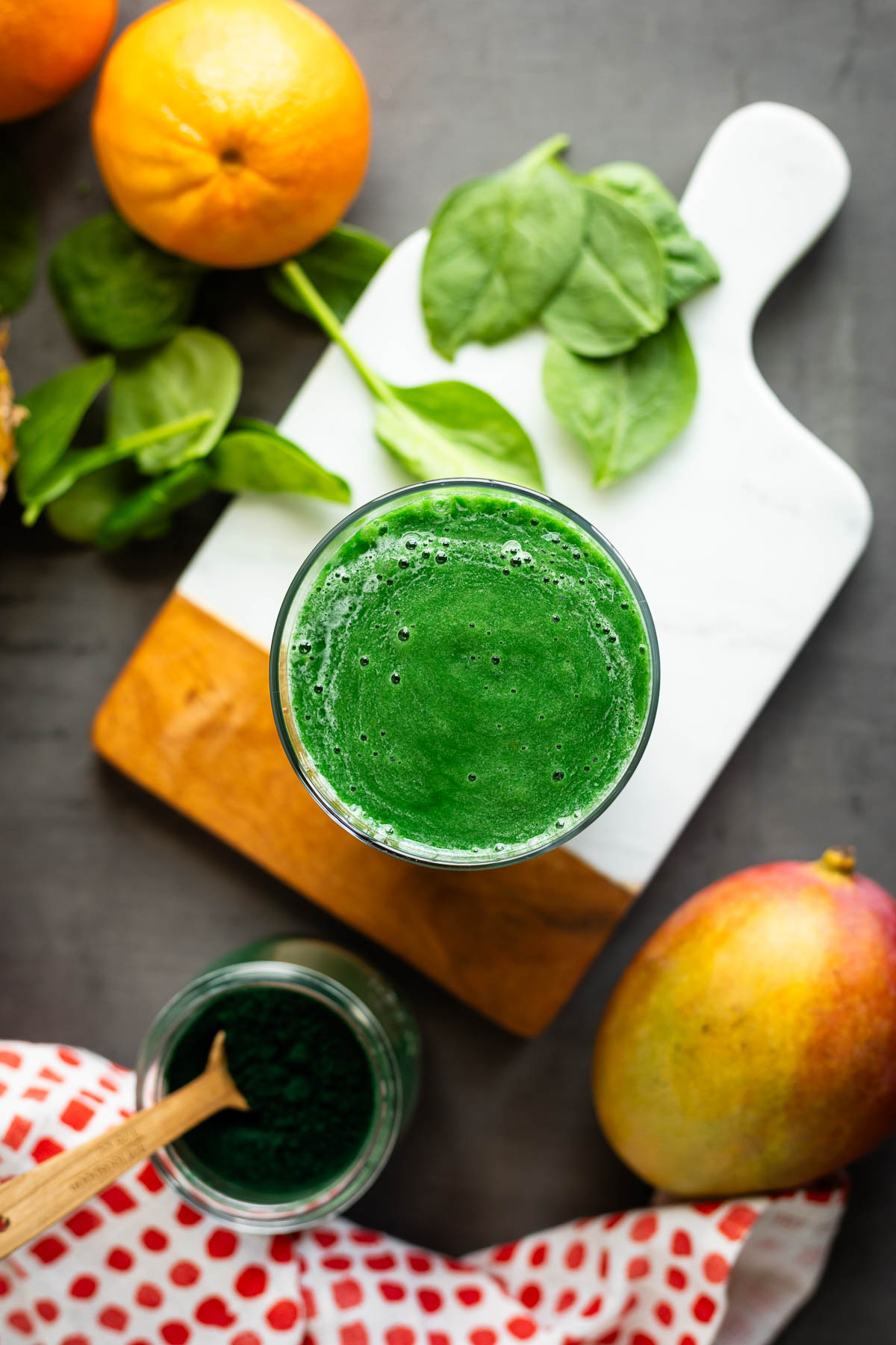 A spirulina smoothie in a glass surrounded by ingredients.