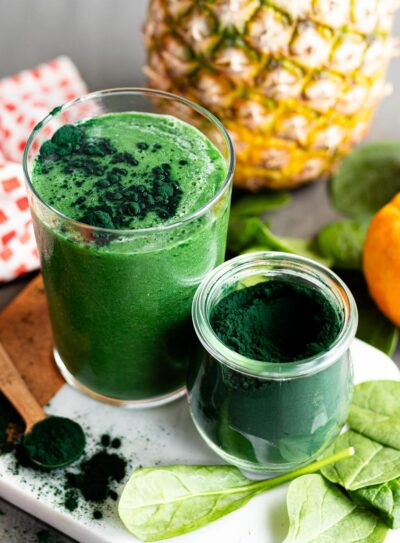 A green spirulina smoothie in a glass beside a jar of spirulina powder.