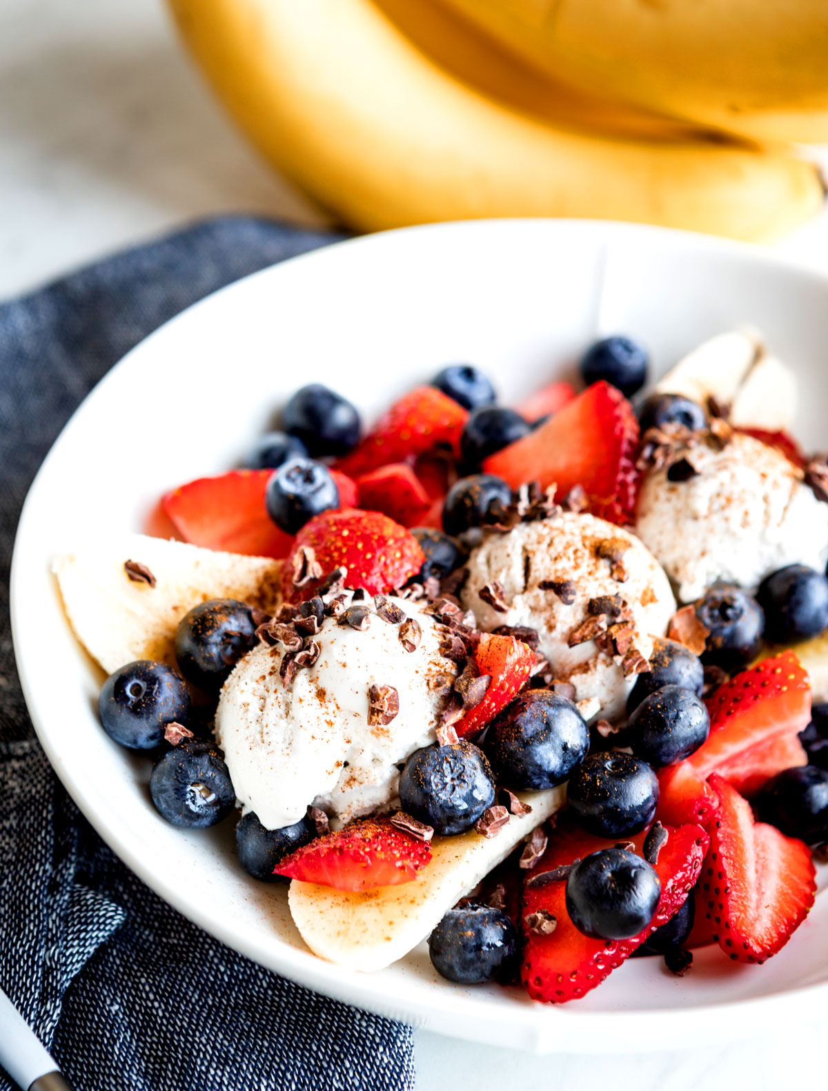 Bowl piled high with strawberries, banana, blueberries and scoop of vegan ice cream.