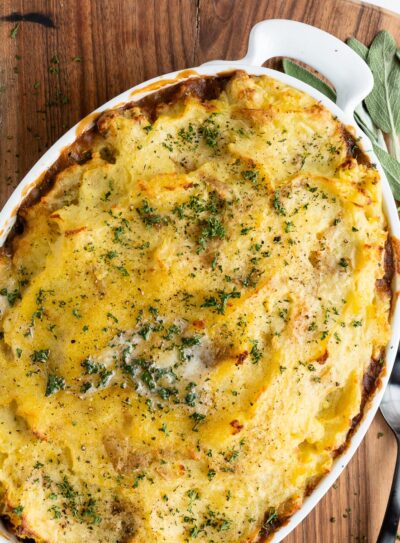 white casserole dish with vegetarian shepherd's pie on a wooden cutting board next to a black serving spoon.