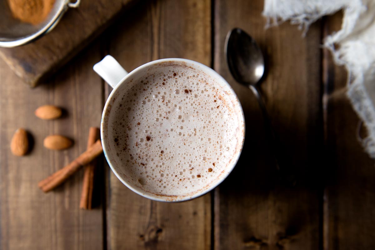 A mug of warm, frothy almond milk topped with a sprinkle of cinnamon and cayenne pepper.