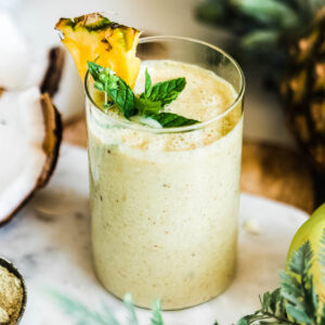 Light yellow smoothie in a glass with a pineapple wedge.