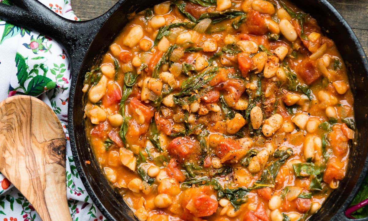 Wooden spoon next to a skillet of beans and vegetables.